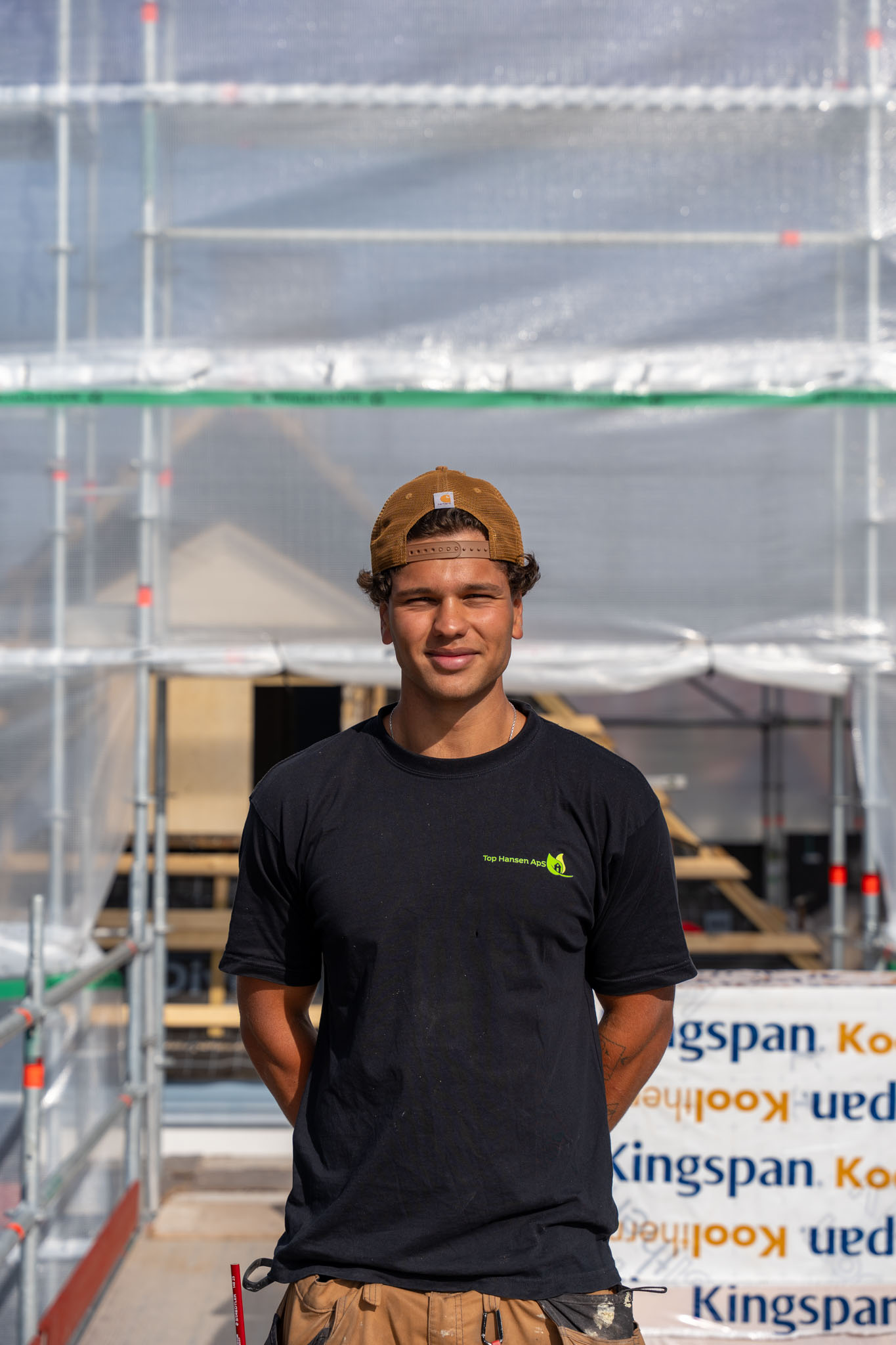 Smilende tømrer fra Top Hansen ApS med brun kasket på stilladset