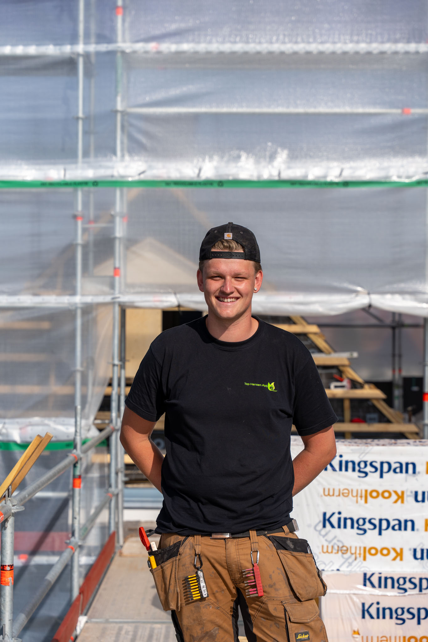 Smilende tømrer fra Top Hansen ApS med sort kasket på stilladset