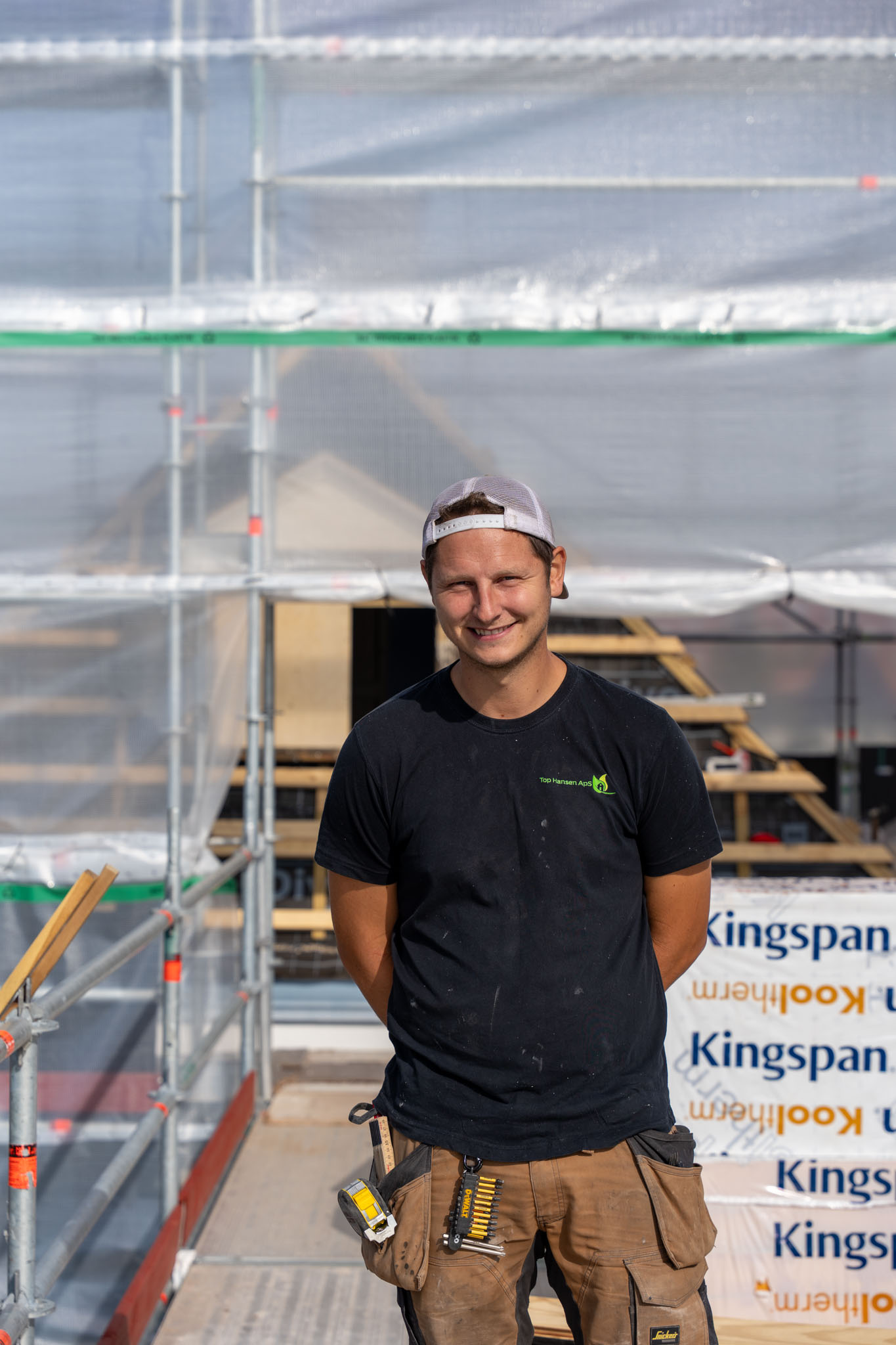 Smilende tømrer fra Top Hansen ApS med lys kasket på stilladset